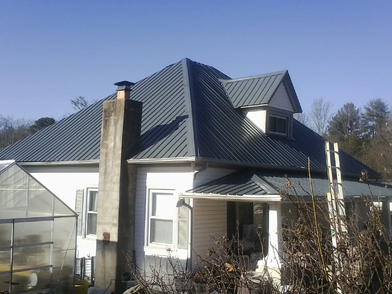 Dark blue standing seam metal roof on a white farmhouse with dormer — Slate & Tile Roof Repair by Roofing Brothers in Lowgap