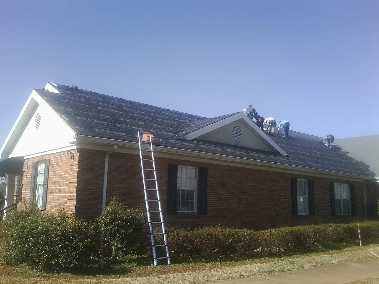 Crew tearing shingles off a brick ranch roof with a ladder set — Metal Roof Repair work by our crew in Lowgap
