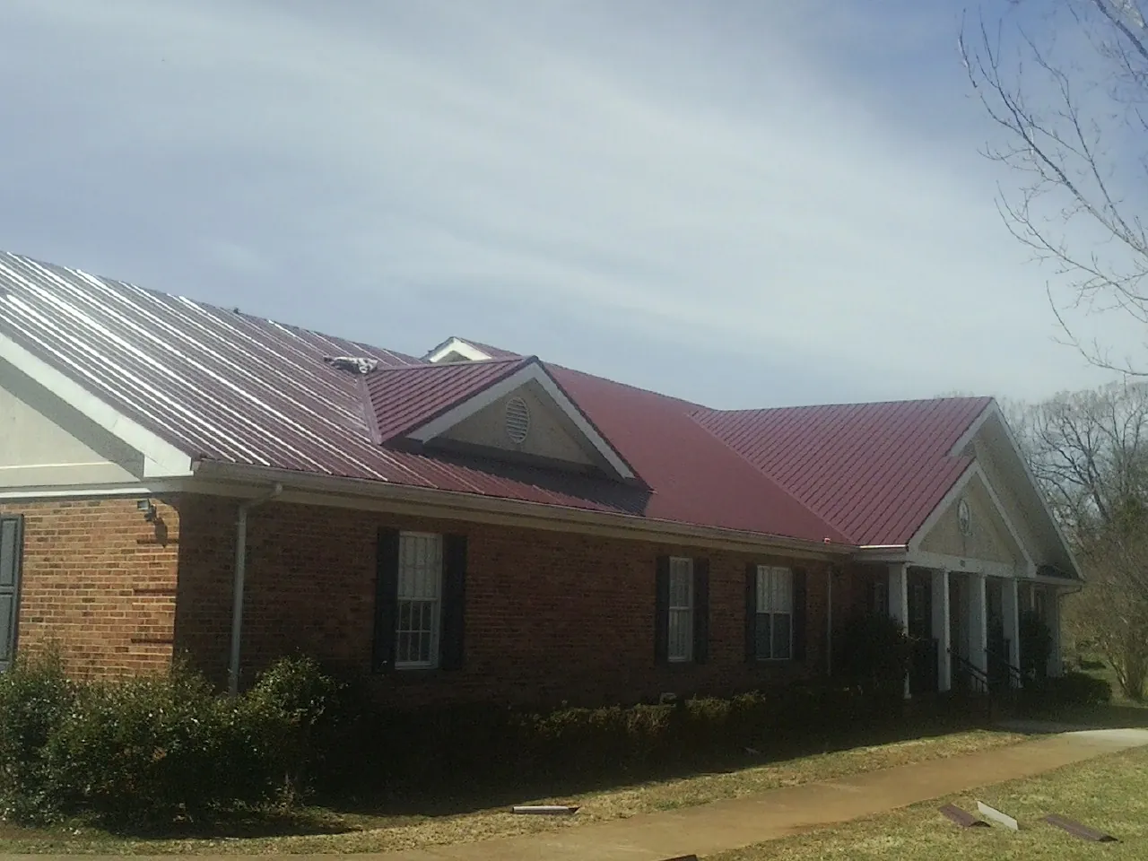 Red metal roof with gabled entries on a long brick building, from a Hail Damage Roof Repair job in Lowgap