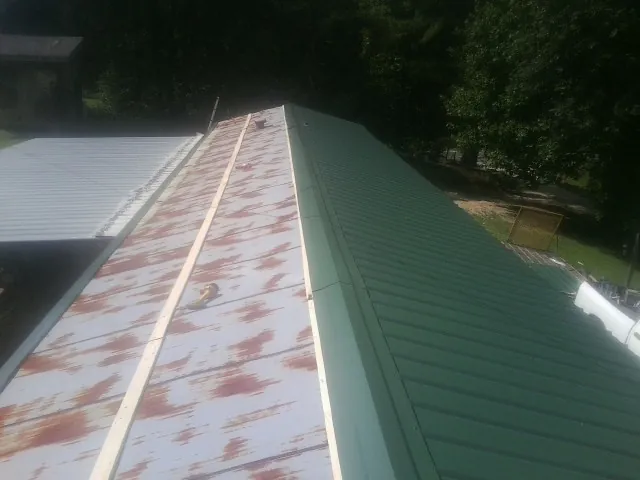 Old rusted panels beside newly installed green metal roofing — Wind Damage Roof Repair by Roofing Brothers in Lowgap