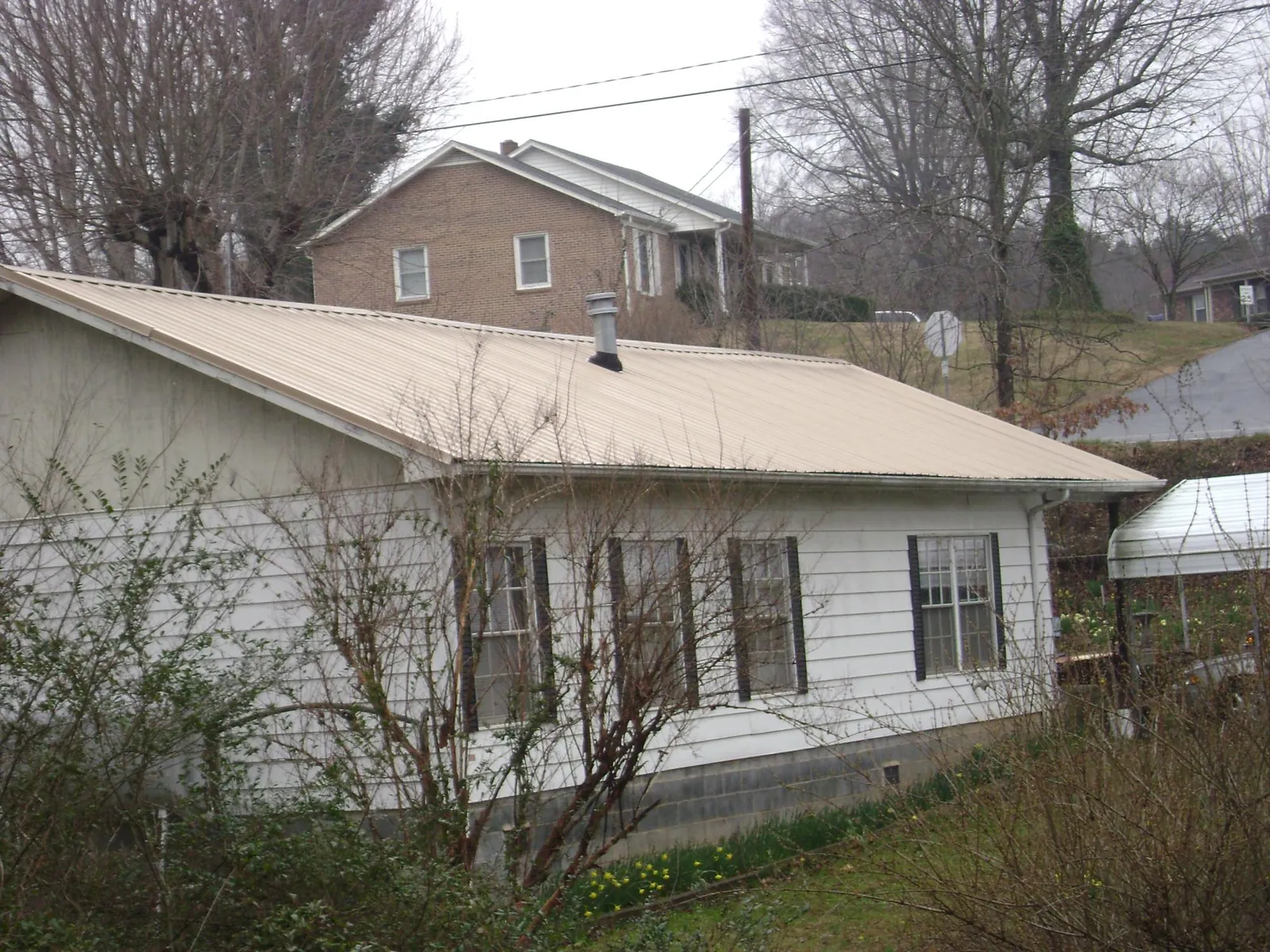 Tan metal roof on a white sided house set into a hillside — Commercial Roofing by Roofing Brothers in Lowgap