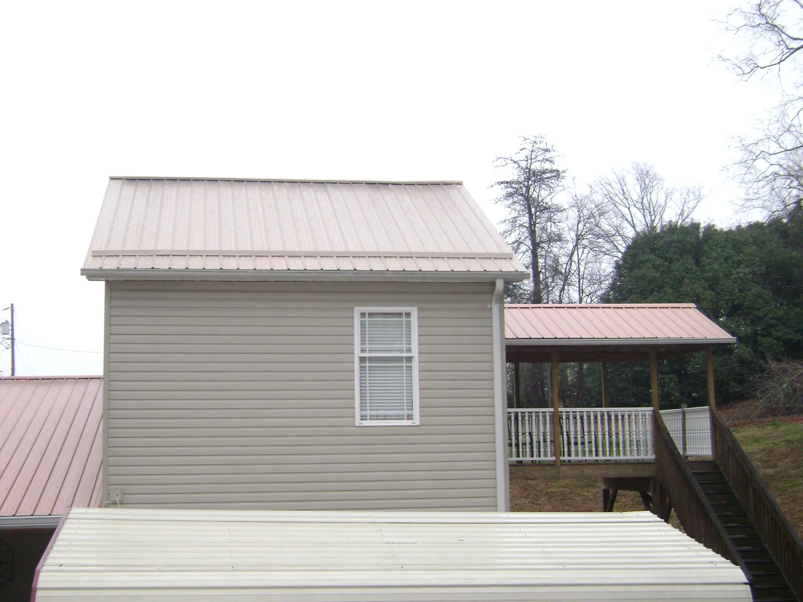 Tan metal roofs on a two story addition and attached porch, from a Roof Replacement job in Lowgap